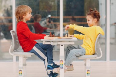 Little couple kids playing chess at kindergarten or elementary school