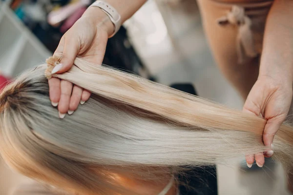 Fryzjer kobieta robi przedłużanie włosów do młodej kobiety z blond włosami w salonie piękności. Profesjonalny kosmyk włosów. — Zdjęcie stockowe