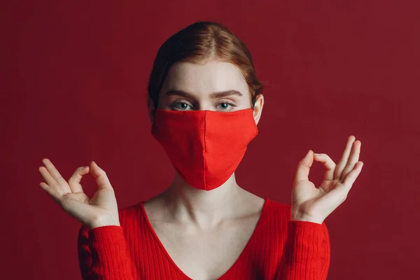 Studio portret van jonge vrouw in beschermende medische gezichtsmasker geïsoleerd op rode achtergrond. Yoga, kalmte, zen en meditatie een covid-19 pandemie concept — Stockfoto