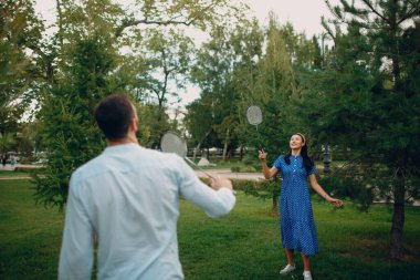Genç bir çift parkta badminton oynuyor.