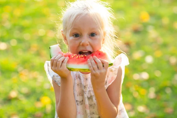Linda menina loira comendo melancia na grama no parque — Fotografia de Stock
