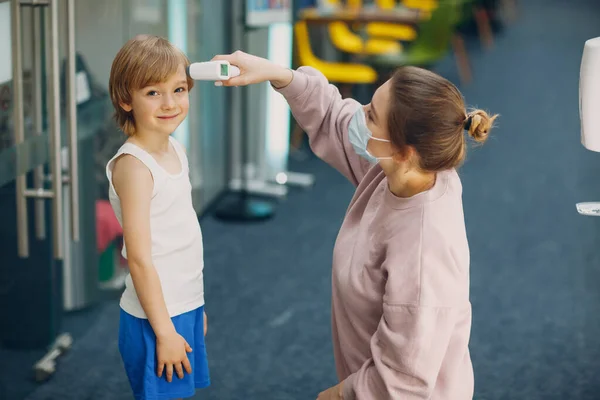 Kind temperatuurmeting vrouw door laser thermometer op kleuterschool. — Stockfoto