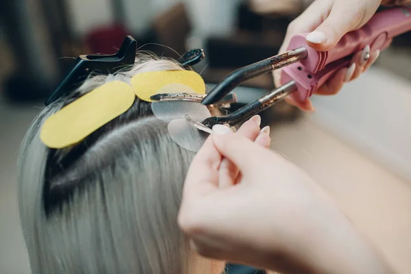 Fryzjer kobieta robi przedłużanie włosów do młodej kobiety z blond włosami w salonie piękności. Profesjonalne przedłużanie włosów. — Zdjęcie stockowe