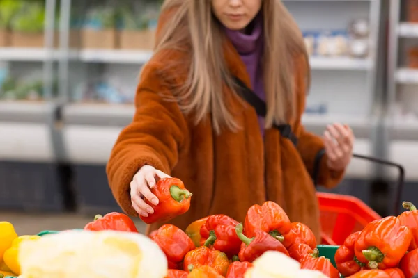 Jovem com uma cesta de supermercado escolhe pimenta vermelha no departamento de vegetais. — Fotografia de Stock
