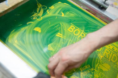Serigraphy silk screen print process at clothes factory. Cleansing Frame, squeegee and plastisol color paints clipart