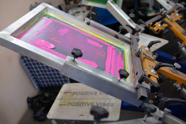 Giyim fabrikasında seri ipek ekran baskı işlemi. Çerçeve, cam sileceği ve plastisol rengi