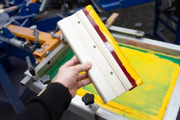 Squeegee for Serigraphy silk screen print process in hand at clothes factory. Frame, squeegee and plastisol color paints