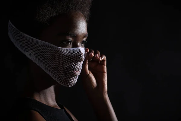 Retrato de primer plano de una mujer afroamericana modelo de moda que usa la máscara de la cara médica de cuarentena malla gruesa sobre fondo negro. Concepto de protección del coronavirus Covid-19. — Foto de Stock