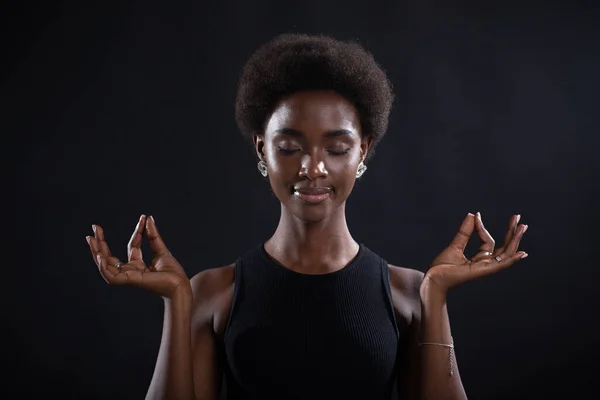 Studio ritratto di modello afro-americano femminile che mostra zen o gesto segno ok. Donna che medita su sfondo nero. — Foto Stock