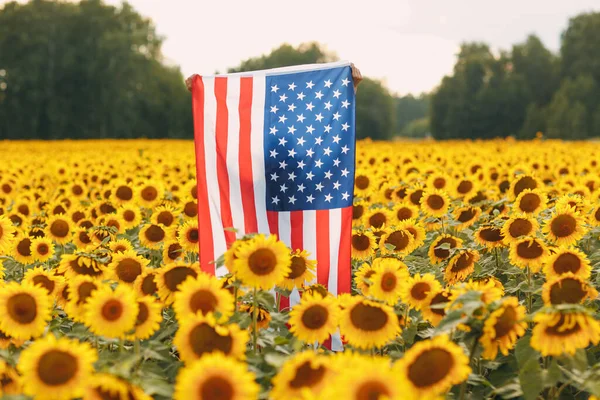 Νεαρή γυναίκα με αμερικανική σημαία στο χωράφι με τα ηλιοτρόπια. 4η Ιουλίου Ημέρα Ανεξαρτησίας ΗΠΑ έννοια. — Φωτογραφία Αρχείου
