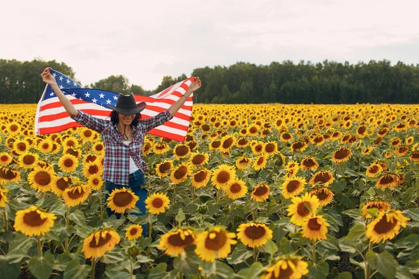 Mujer joven con bandera americana en el campo de girasol. 4 de julio Día de la Independencia USA concepto. — Foto de Stock