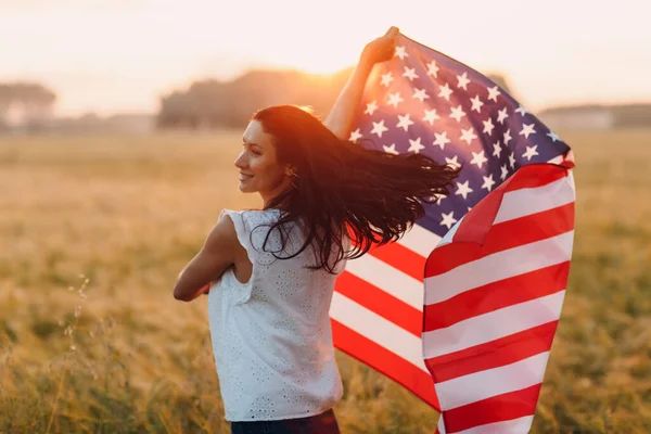 Mujer agricultora en el campo agrícola con bandera americana al atardecer — Foto de Stock