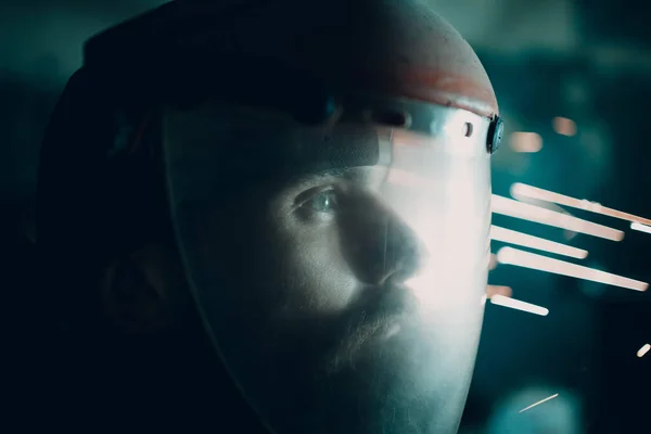 Hombre amoladora soldadora en máscara protectora transparente con chispas voladoras en la oscuridad. — Foto de Stock