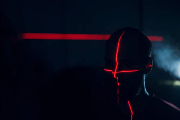 Hombre en la oscuridad con la cara iluminada por el escaneo láser rojo en el contorno — Foto de Stock