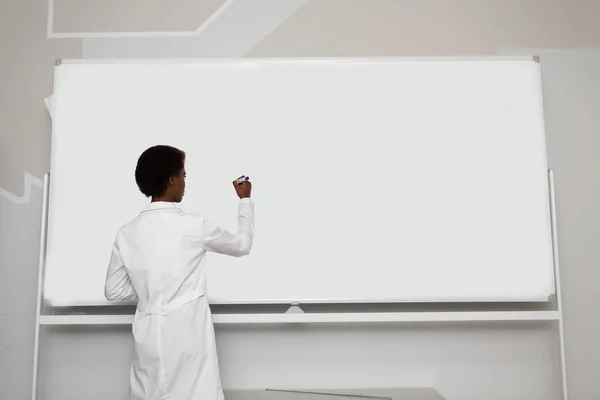 African American woman math teacher stands at blackboard with marker