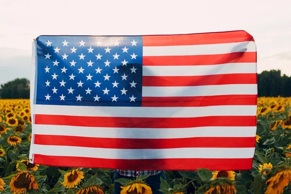 Mujer joven con bandera americana en el campo de girasol. 4 de julio Día de la Independencia USA concepto. — Foto de Stock