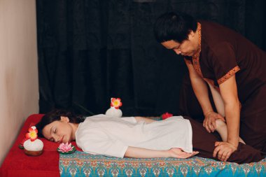 Taylandlı adam güzellik merkezinde genç bir kadına klasik Tayland masajı yapıyor.