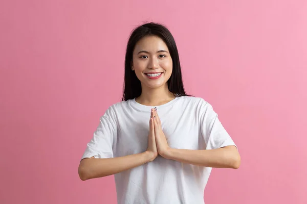 Namaste Portret Azjatki trzymającej się za ręce i kłaniającej się azjatyckim gestem powitania na różowym tle. — Zdjęcie stockowe