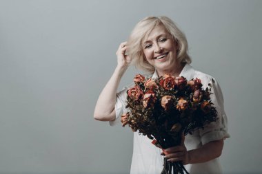 Olumlu gülümseyen yaşlı kadın elinde gül çiçeği buketi.