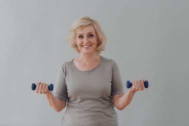 Yaşlı, beyaz, yaşlı kadın portresi gri saçlı, dambıllarla egzersiz yapıyor..