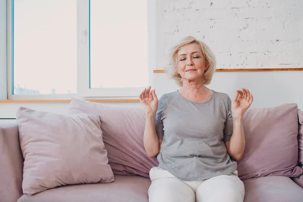 Wanita tersenyum senior sedang berlatih yoga di ruang keluarga. Wanita tua santai duduk di berpose teratai dan meditasi zen seperti. — Stok Foto