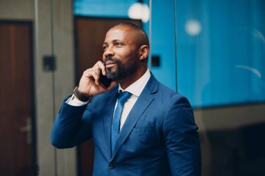 Mavi takım elbiseli Afro-Amerikan işadamı gülümseyen bir portre cep telefonuyla konuşuyor..