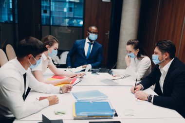 İş adamı ve iş kadını ekibi, ofis toplantısında tıbbi maske takıyor. Patronla iş adamları grup toplantısı.