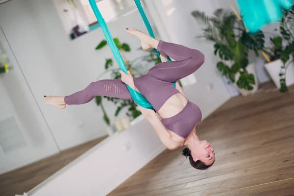 Woman doing aerial yoga in studio. Female practicing air yoga in hammock