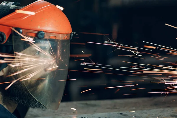 Pekerja dengan topeng pelindung transparan bekerja pada logam dengan gergaji penggiling melingkar. Sparks dan wajah. — Stok Foto