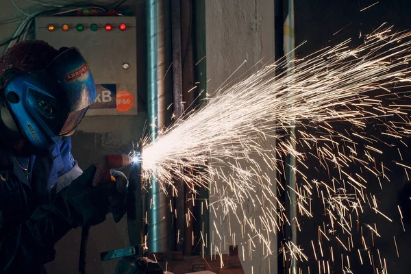 Man in mask cuts metal with plasma cutter. Helmet and spakrs