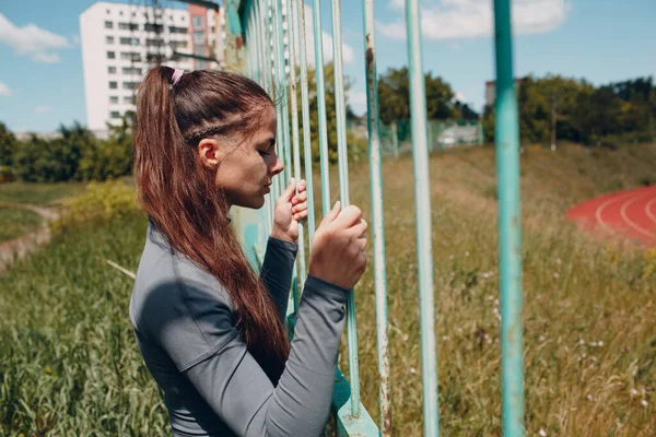 Gadis itu memanjat pagar stadion. Wanita muda olahraga akan menjalankan pelatihan. — Stok Foto