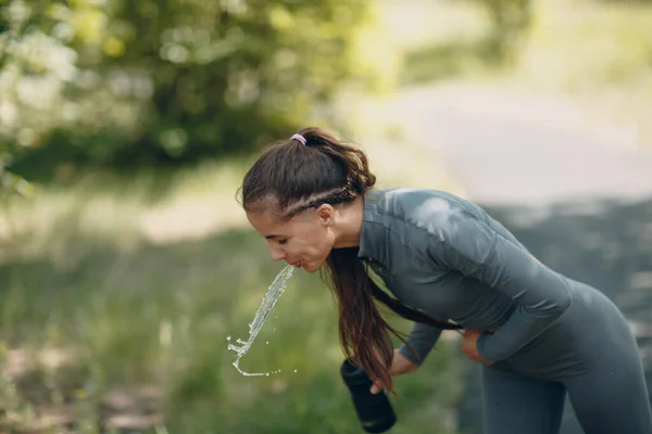 Fáradt futó nő kocogó ivás palackozott víz után kocogás a parkban szabadban. — Stock Fotó