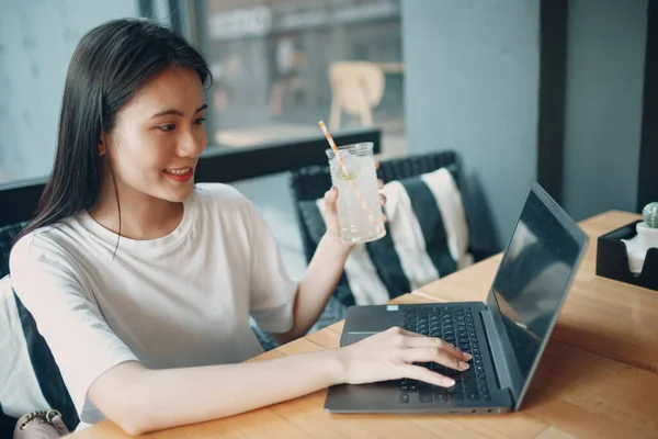 Азиатская девушка пьет лимонадную соду и пользуется ноутбуком в кафе на открытом воздухе — стоковое фото