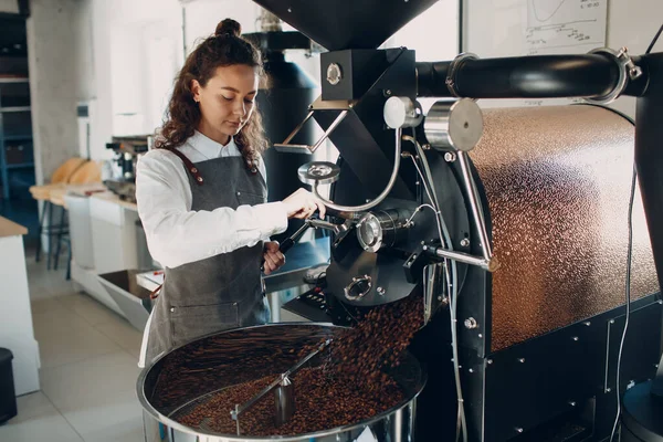 Coffee cooling in roaster machine at coffee roasting process. Young woman worker barista Mixing coffee beans.