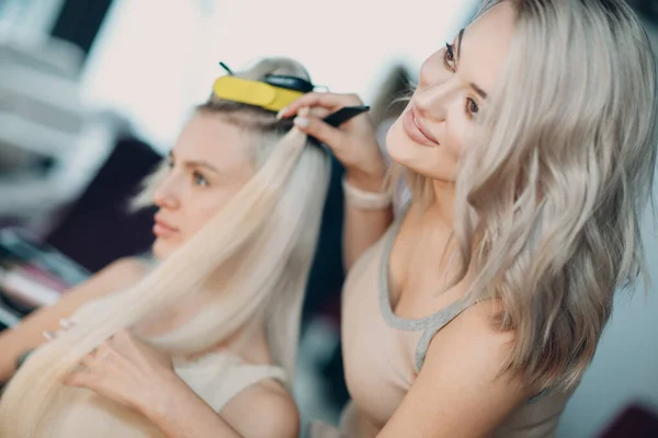 Cabeleireiro feminino fazendo extensões de cabelo para jovem mulher com cabelo loiro no salão de beleza. Extensão profissional do cabelo. — Fotografia de Stock