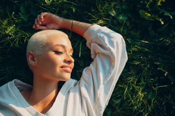 Millenial junge Frau blonde kurze Haare im Freien lächelnd lag auf Gras Porträt. — Stockfoto