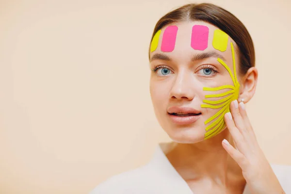 Beautiful woman applying tape lifting treatment on face