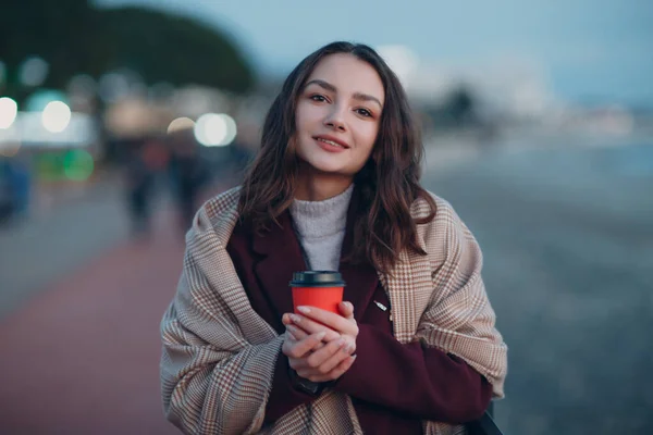 코트를 입고 스카프를 두른 아름다운 여인 과 커피 잔을 들고 야외에 나가 있는 모습. — 스톡 사진