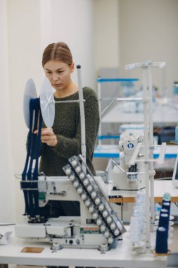 Genç, güzel terzi fabrikadaki dikiş makinesine dikiş dikiyor.