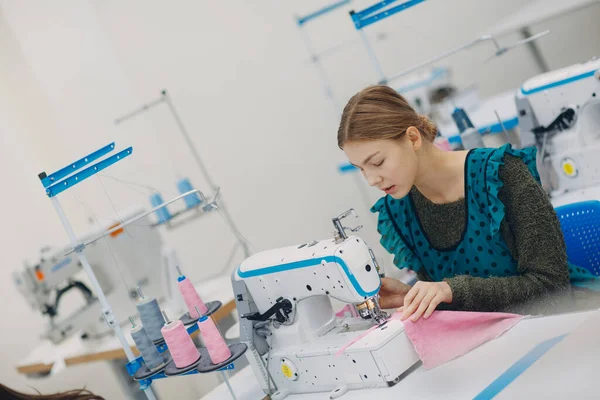 Young beautiful seamstress sews on sewing machine in factory