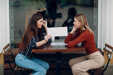 Elinde beyaz kağıt tutan bir kadın. Caddedeki kafede konuşan iki kadın. Boş boşluklu beyaz şablon sayfası.