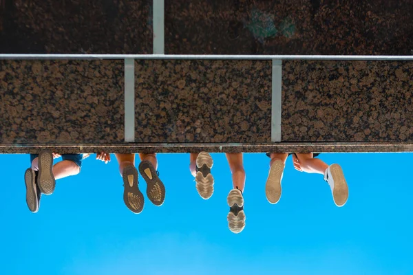 Garçons jambes dans des chaussures suspendues au pont contre le ciel bleu — Photo