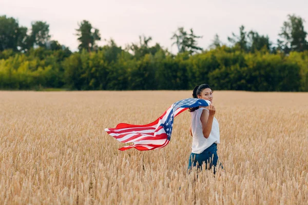 Γυναίκα με αμερικανική σημαία σε χωράφι με σιτάρι το ηλιοβασίλεμα. 4 Ιουλίου. Ημέρα Ανεξαρτησίας. — Φωτογραφία Αρχείου