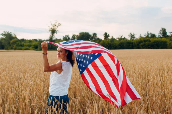 Mujer con bandera americana en el campo de trigo al atardecer. 4 de julio. Día de la Independencia fiesta patriótica. — Foto de Stock