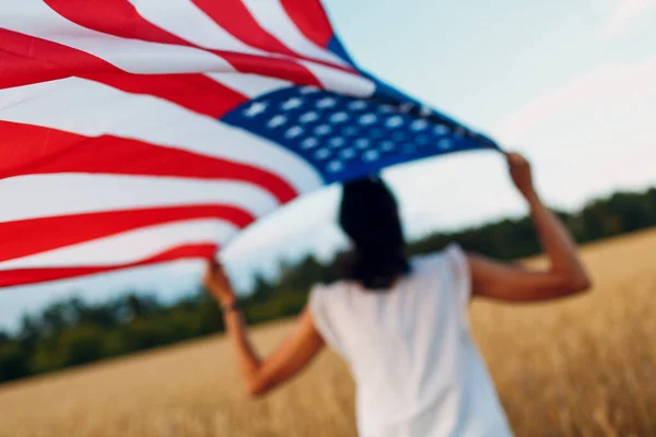 Mujer con bandera americana en el campo de trigo al atardecer. 4 de julio. Día de la Independencia fiesta patriótica. — Foto de Stock