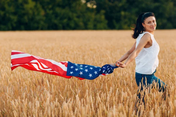 Woman with American flag in wheat field at sunset. 4th of July. Independence Day patriotic holiday. — Stock Photo, Image