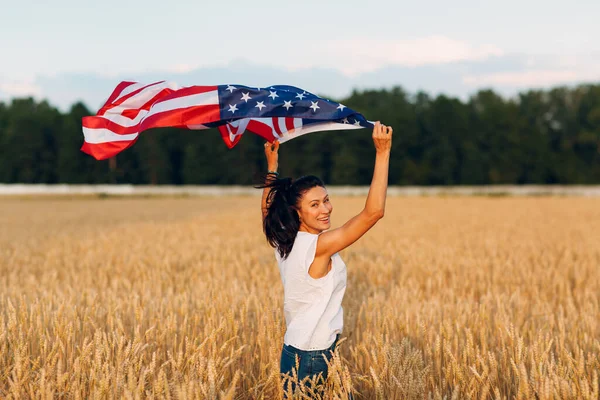 Γυναίκα με αμερικανική σημαία σε χωράφι με σιτάρι το ηλιοβασίλεμα. 4 Ιουλίου. Ημέρα Ανεξαρτησίας. — Φωτογραφία Αρχείου