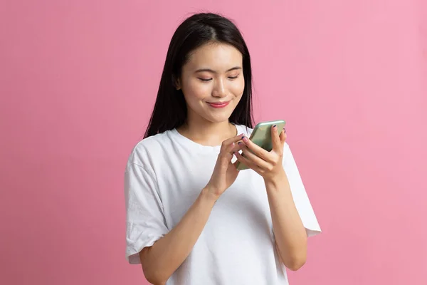 Улыбающаяся азиатка указывает на смартфон, стоящий на розовом фоне. — стоковое фото