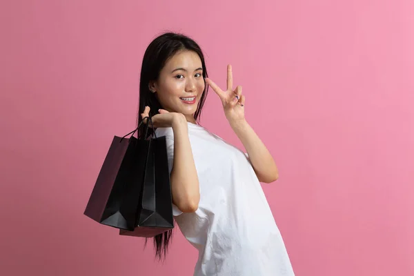 Compras asiático feliz mulher segurando sacos de compras no fundo rosa — Fotografia de Stock