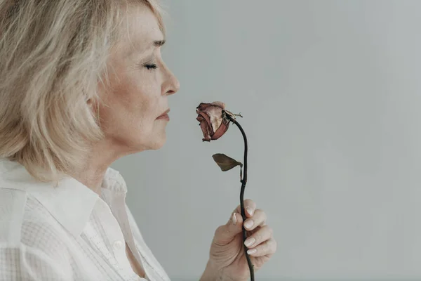 Kesal tua wanita berpakaian putih layu satu bunga mawar tua kering. — Stok Foto